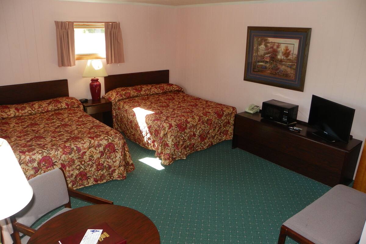 A hotel room with two beds, a desk with a television, a lamp, and a painting on the wall.