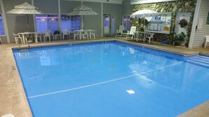 An indoor swimming pool with clear blue water, surrounded by white lounge chairs and umbrellas.