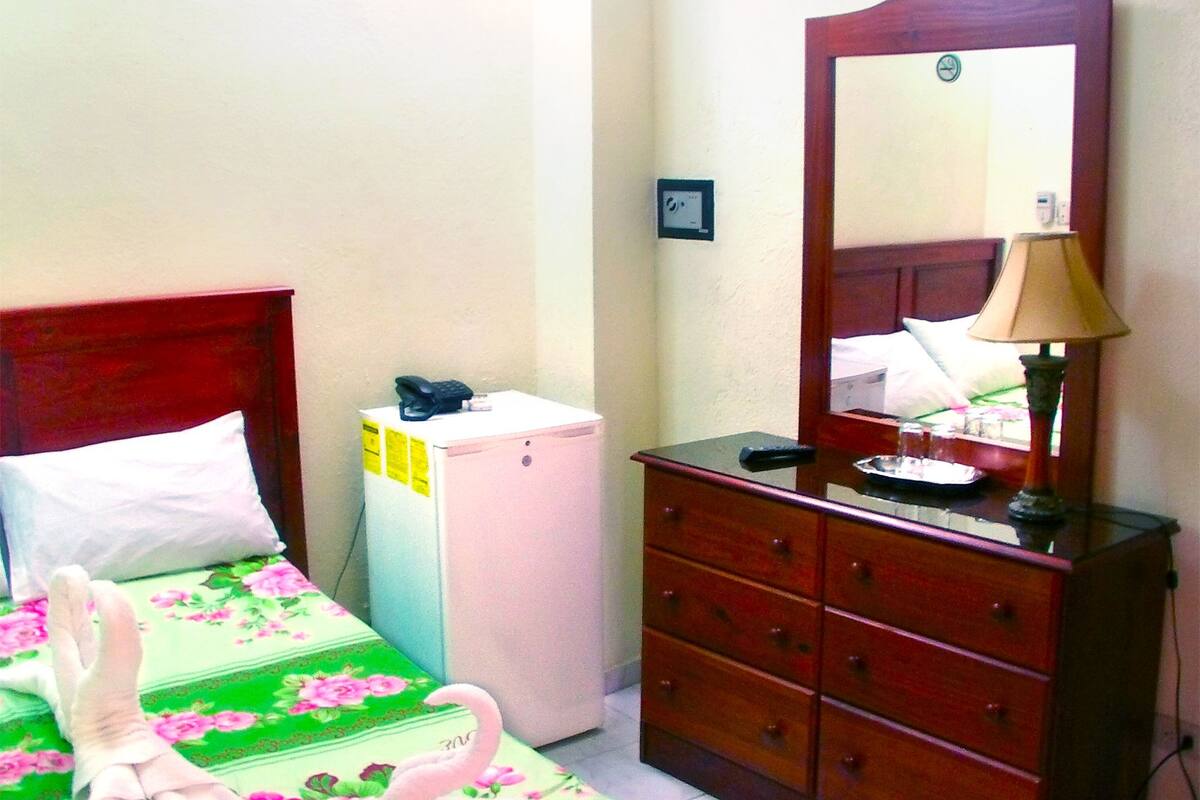 Een slaapkamer met een bed, een dressoir, een spiegel en een kleine koelkast.