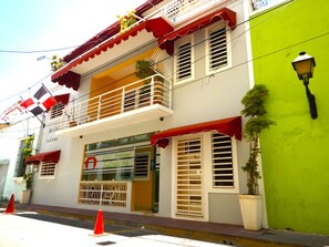 Um hotel com fachada vermelha e branca, varandas com grades brancas e uma parede verde em um dos lados.