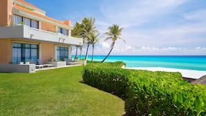A modern beachfront property with a white exterior, large windows, and a well-maintained lawn.