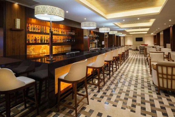 A bar area with a long counter, multiple bar stools, and a patterned floor.
