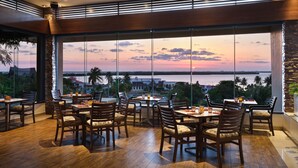 A restaurant with a view of the sunset over water, featuring wooden furniture and large windows.