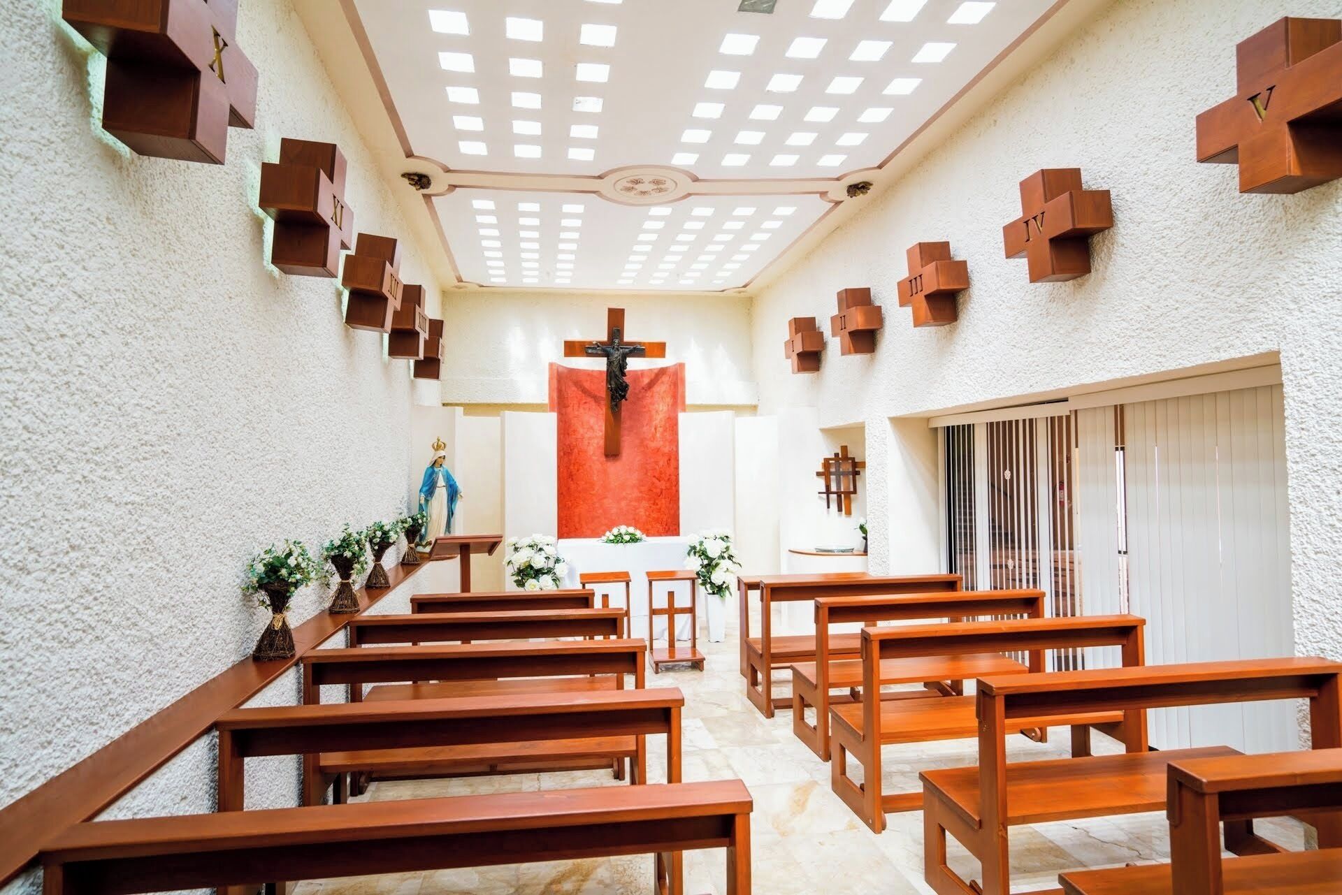 A church interior with wooden pews, a crucifix, and a statue of the Virgin Mary.