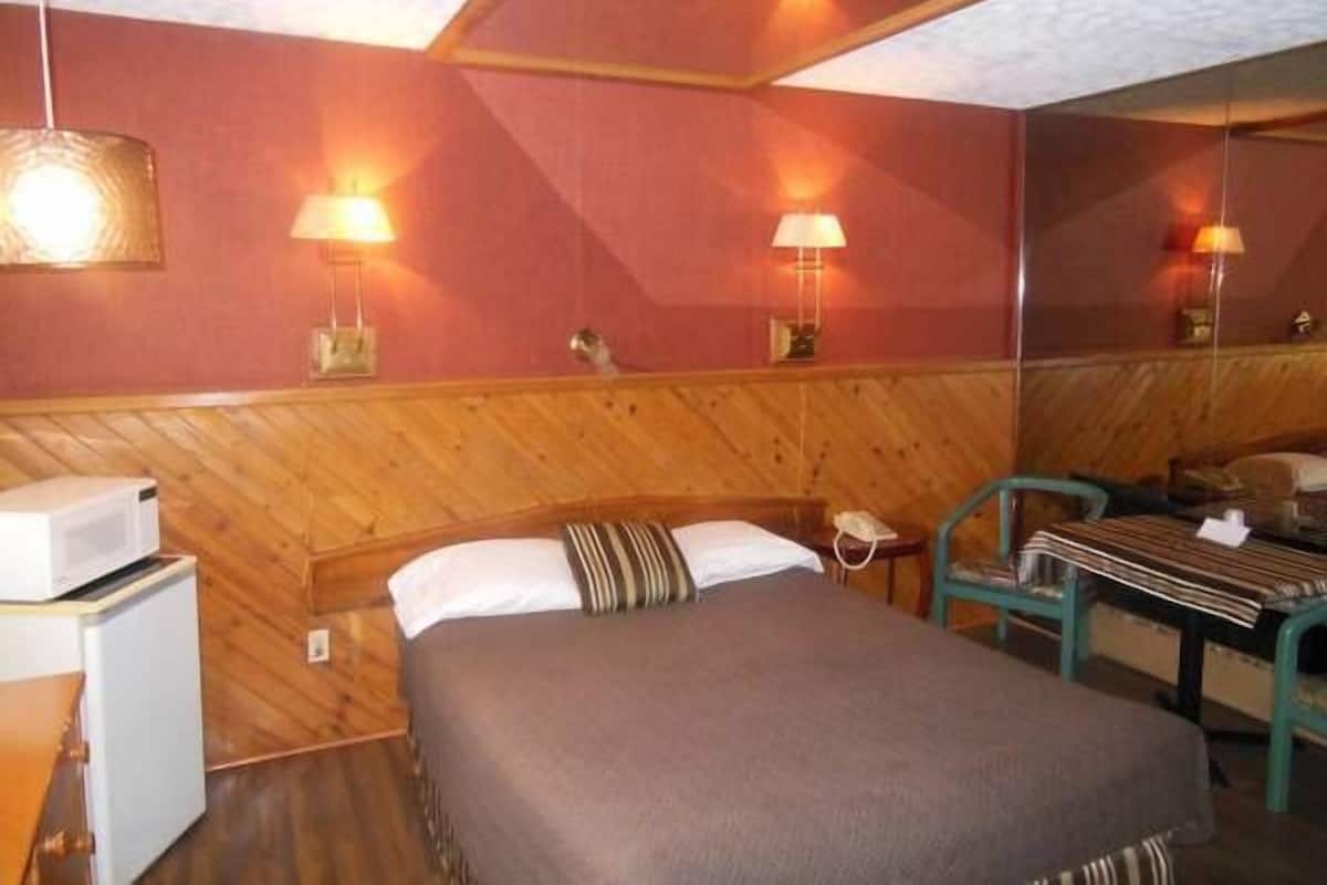 Ein Hotelzimmer mit einem Bett, einem Schreibtisch und einem Stuhl. Zwei Wandlampen und ein Kühlschrank sind vorhanden.