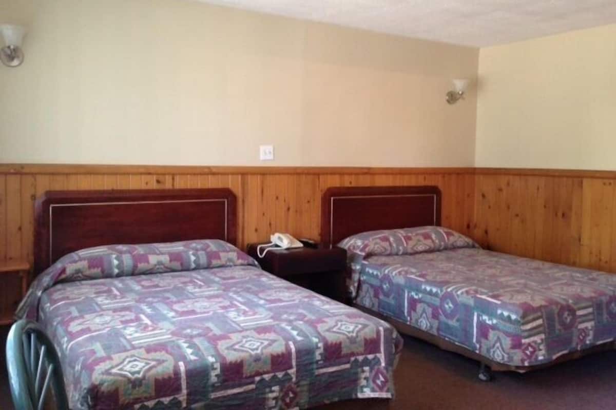 Ein Zimmer mit zwei Betten, Holzvertäfelung an den Wänden und einem kleinen Nachttisch mit Telefon.
