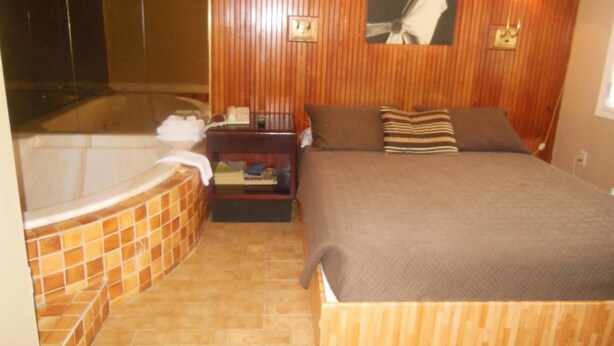 Un dormitorio con una cama grande, un cabecero de madera, una mesita de noche, una lámpara y un cuadro colgado en la pared.