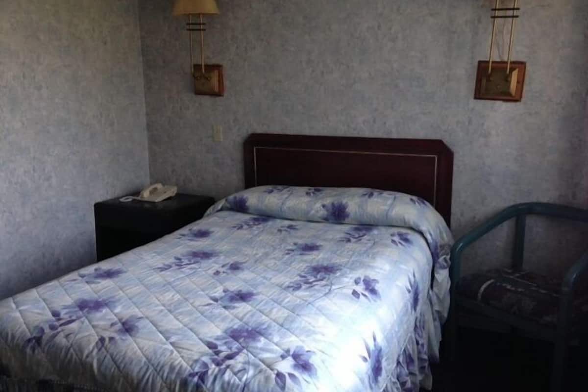 Ein Einzelbett mit blumigem Überwurf, ein hölzernes Kopfteil, zwei Nachttische mit Lampen und ein Sessel.