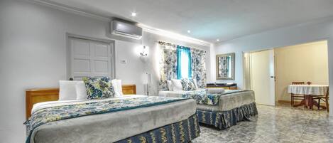 A hotel room with two beds, a dining area, and a bathroom.