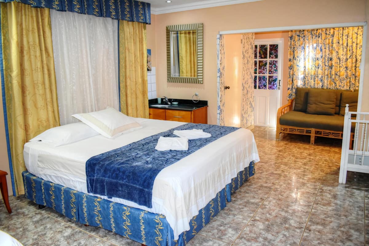 A bedroom with a bed, a nightstand, a chair, and a bathroom with a sink and mirror.