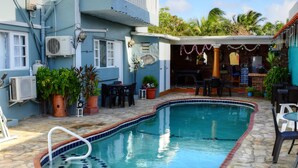 A swimming pool with a stone border and a blue tiled edge, surrounded by outdoor furniture and potted plants.