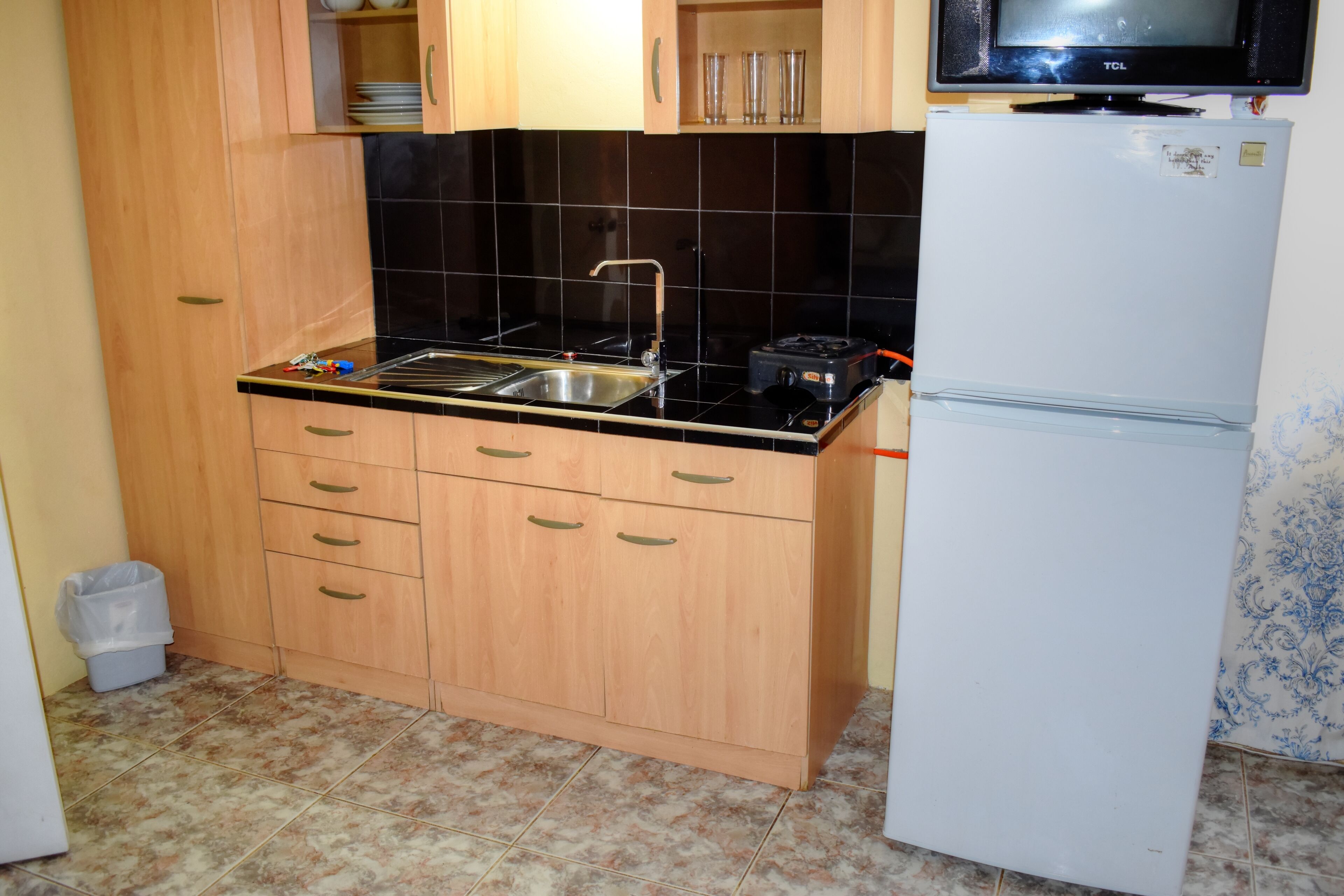 A compact kitchen with wooden cabinets, a black countertop, a sink, a stove, and a white refrigerator.