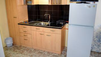 A compact kitchen with wooden cabinets, a black countertop, a sink, a stove, and a white refrigerator.