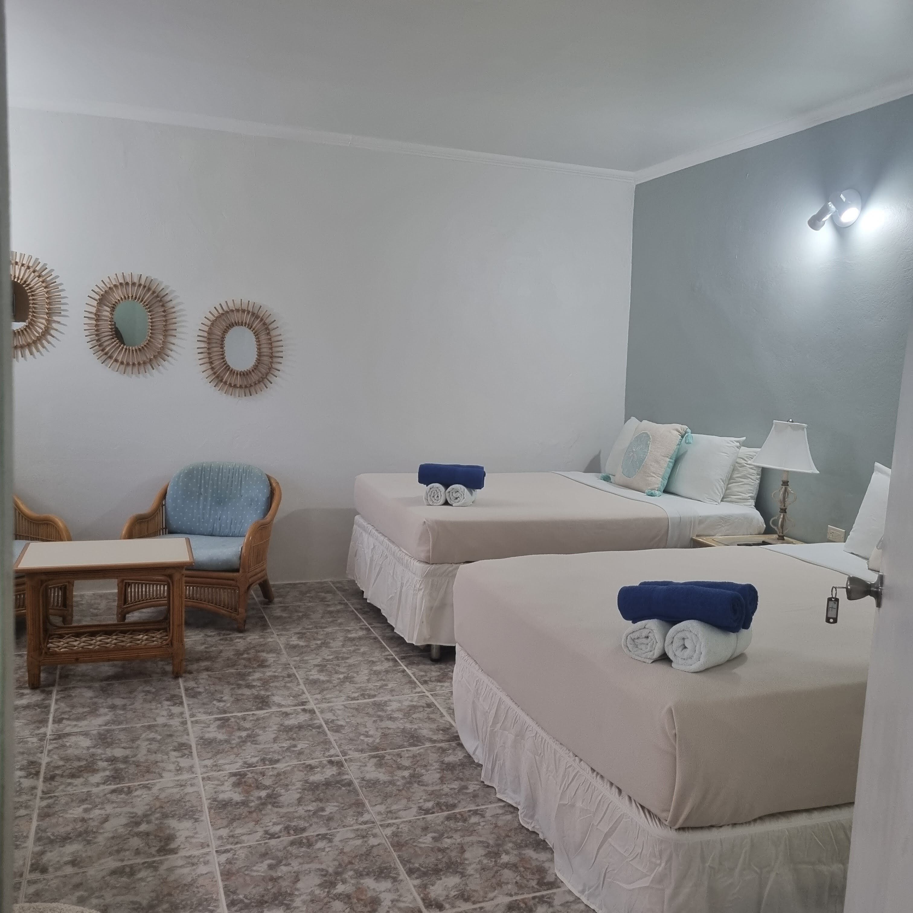 Habitación de hotel con dos camas, una silla, una mesita y espejos decorativos en la pared.