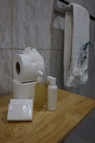 Un baño con tocador de madera, un rollo de papel higiénico, dos botellas de jabón líquido y una toalla blanca doblada.