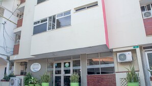 A hotel entrance with a signboard, potted plants, and an air conditioning unit.