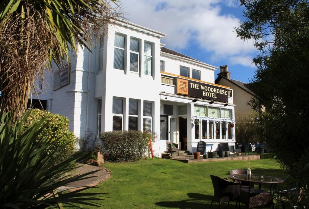 A two-story building with a sign reading 'The Woodhouse Hotel.' There is a lawn in front with a table and chairs.