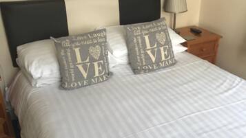 Una cama bien tendida con dos almohadas decorativas, una mesita de noche con una lámpara y una obra de arte en la pared.
