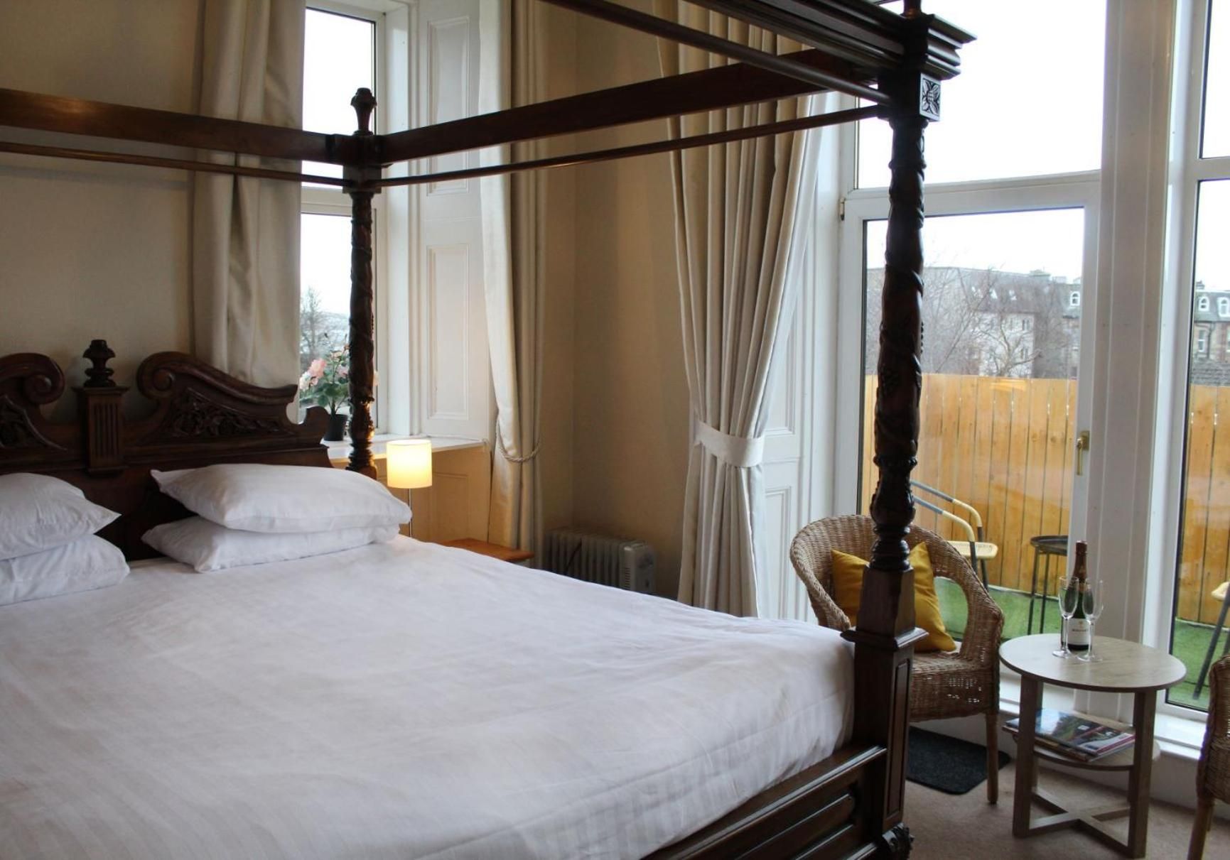 Una cama con dosel con ropa blanca, un cabecero de madera y vista a un jardín cercado a través de una ventana.
