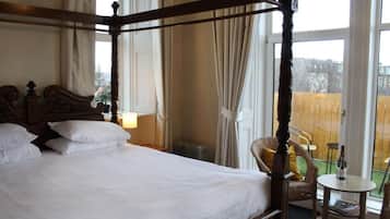 Una cama con dosel con ropa blanca, un cabecero de madera y vista a un jardín cercado a través de una ventana.
