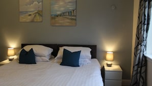 A neatly made bed with white linens and two dark blue pillows, flanked by two bedside lamps on white nightstands. - The Woodhouse Hotel (Largs)