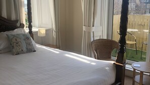 A four-poster bed with a white bedspread, a decorative pillow, and a wicker chair by a window. - The Woodhouse Hotel (Largs)