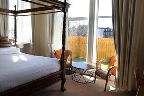A four-poster bed with a view of a wooden deck through a window. - The Woodhouse Hotel (Largs)