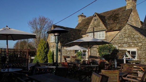 An outdoor seating area with tables and chairs, umbrellas, and a stone building in the background. - The Tollgate Inn (Trowbridge)