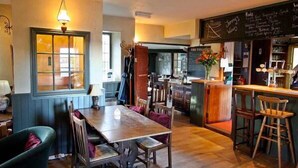 A cozy restaurant with a wooden dining table, chairs, and a bar area. - The Tollgate Inn (Trowbridge)