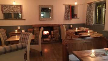 A cozy room with a stone fireplace, wooden furniture, and a view of the outside through a window.