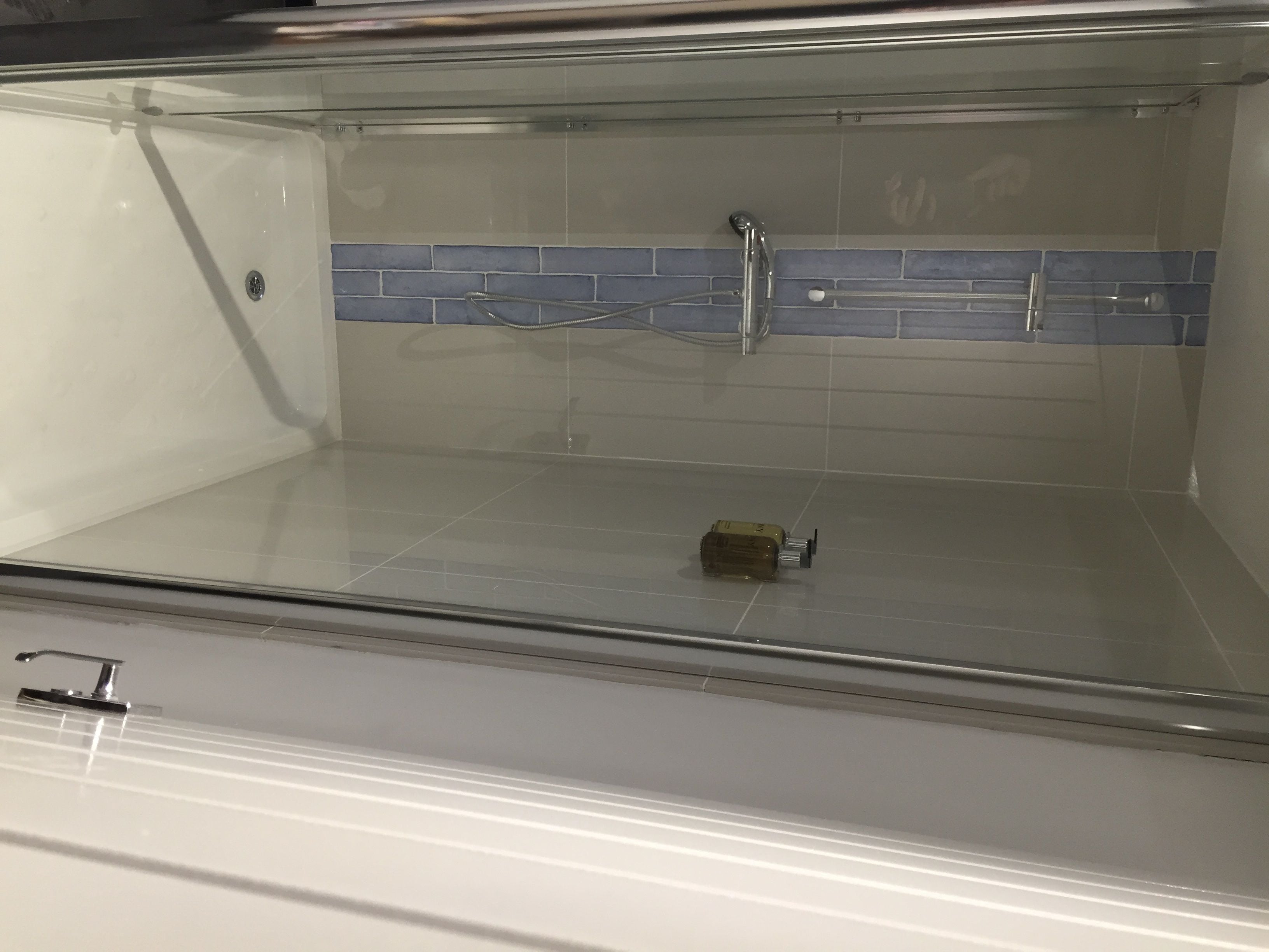 Un bagno con cabina doccia in vetro, doccia dotata di soffione manuale e parete rivestita di piastrelle a motivi blu e bianchi.