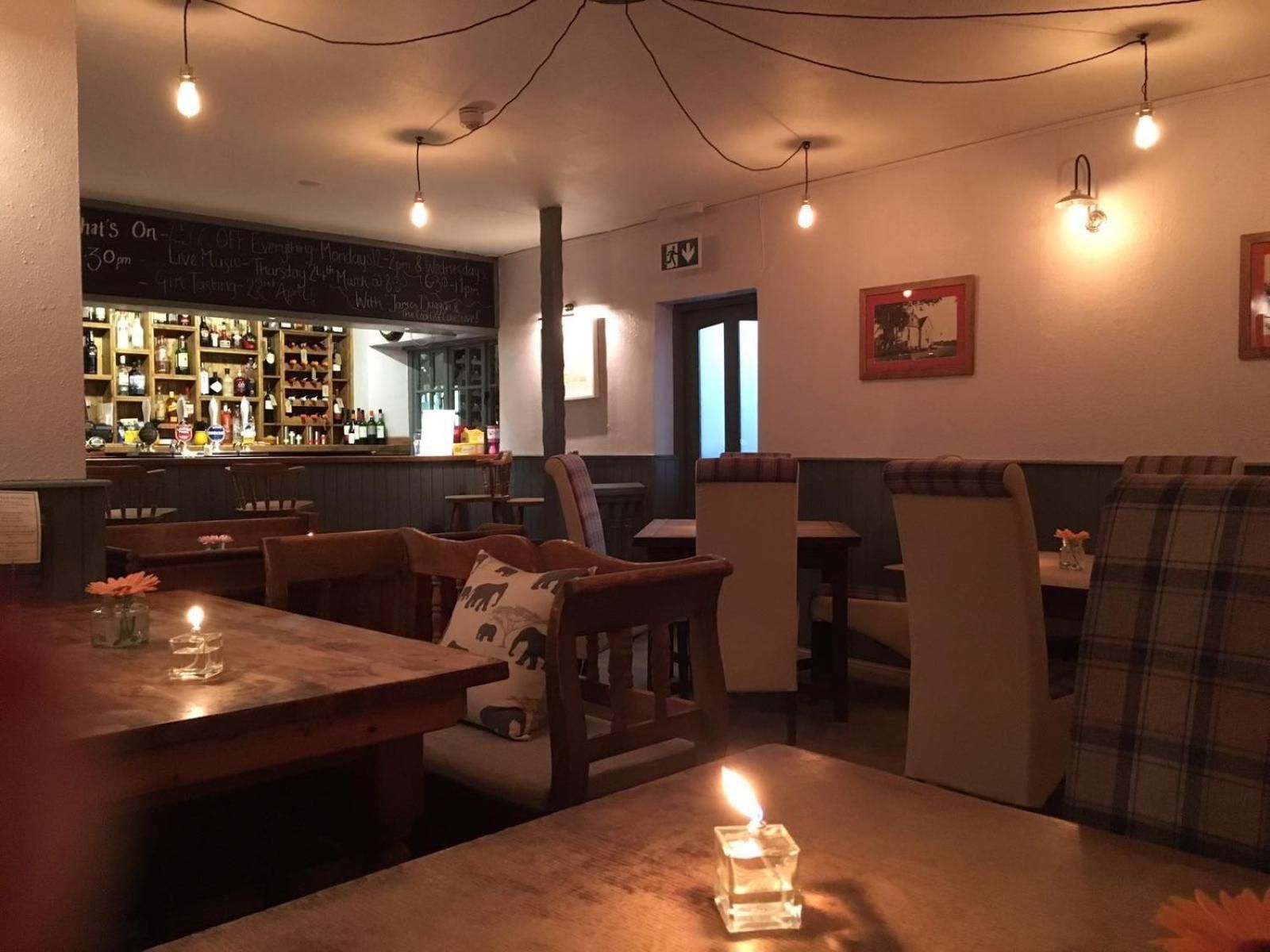 A cozy restaurant interior with wooden tables and chairs, a bar area with shelves of bottles, and a chalkboard menu.