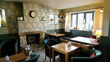 Um pub acolhedor com lareira, papel de parede floral e uma janela com cortinas.