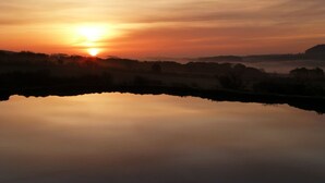 A serene sunrise over a calm lake with a misty landscape in the background. - The Grainary Farm Stay (Scarborough)