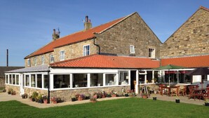 A stone building with a red-tiled roof, a covered patio area with outdoor seating, and a well-maintained lawn. - The Grainary Farm Stay (Scarborough)