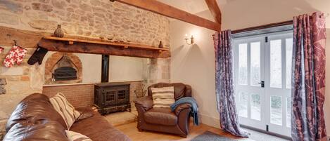 A cozy living room with a stone fireplace, leather sofa, and a large window with curtains.