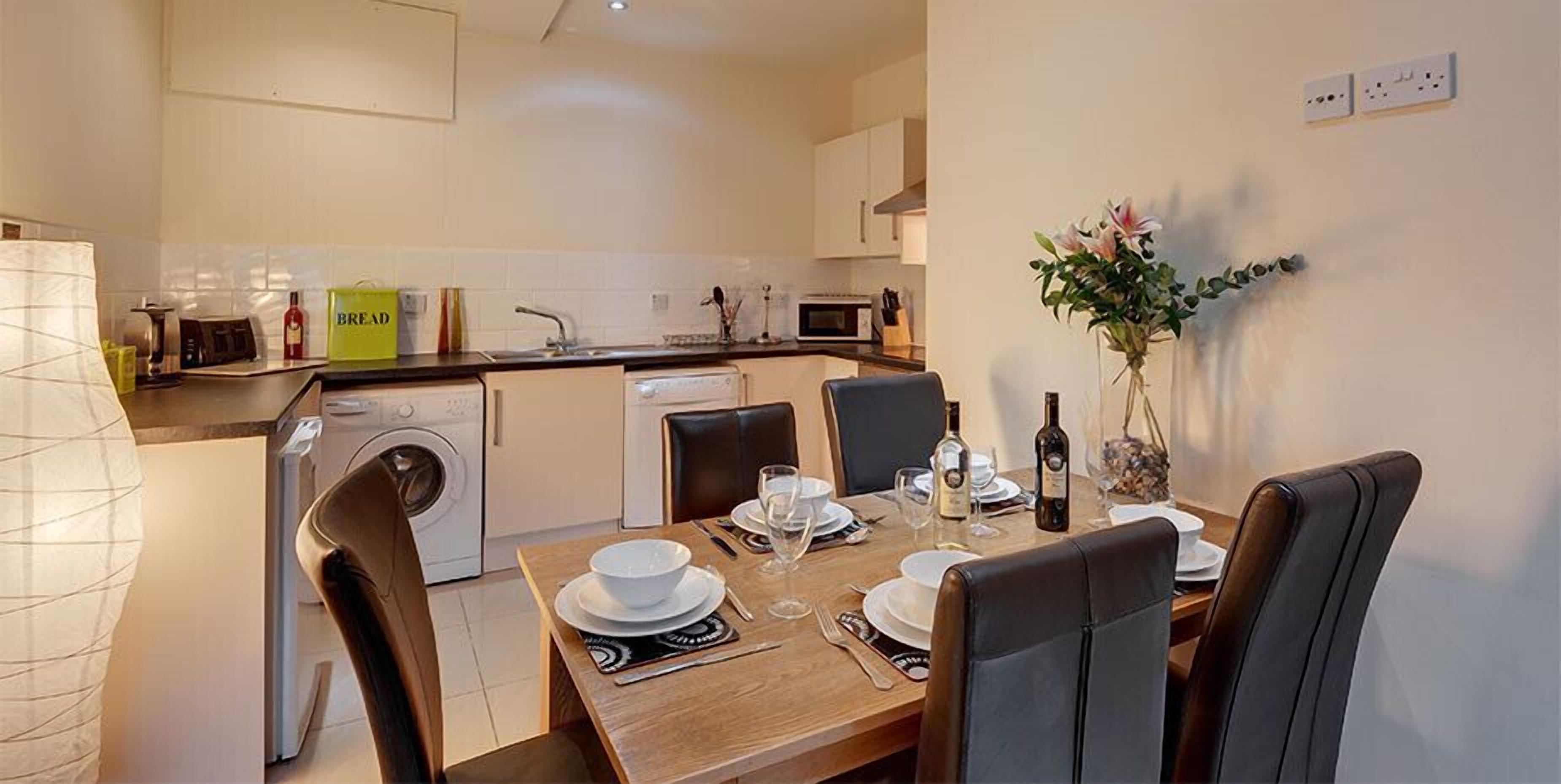 A compact kitchen with a dining area, including a table set for two with plates, glasses, and a bottle.