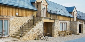 A stone building with wooden exterior walls, a staircase leading to a balcony, and outdoor seating.
