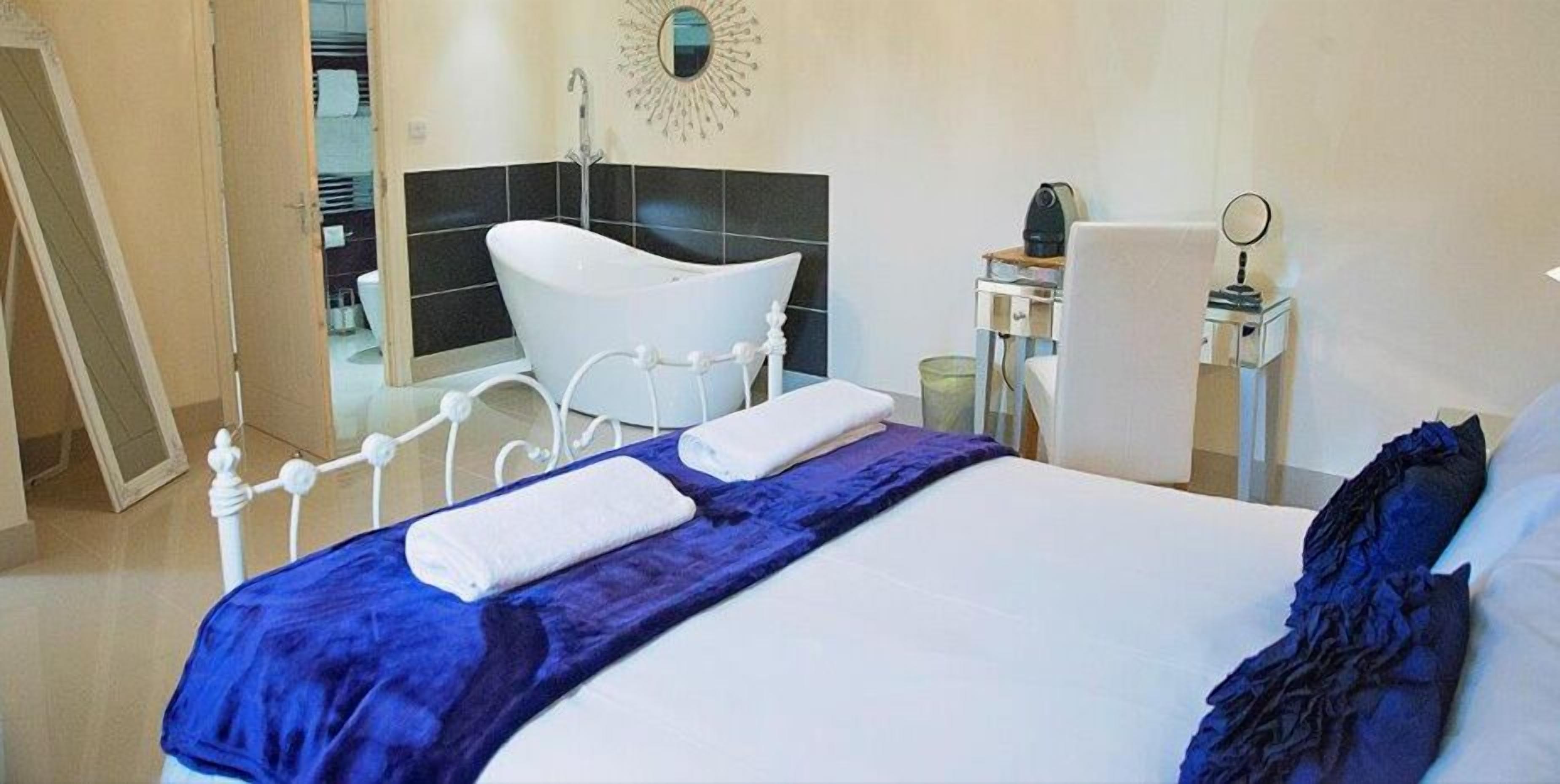 A hotel room with a bed, a white bathtub, a desk with a chair, and a mirror.