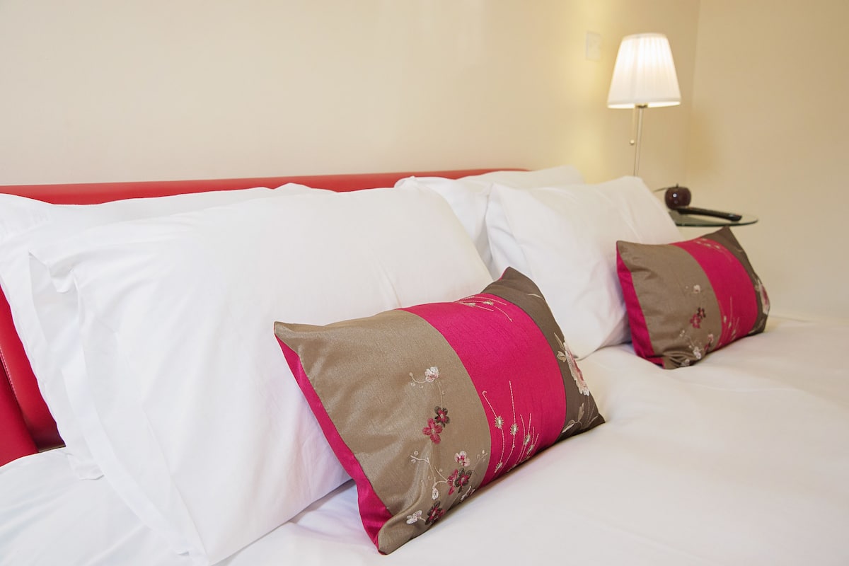 Una cama bien hecha con almohadas blancas y marrones, cabecera roja y una lámpara de noche.