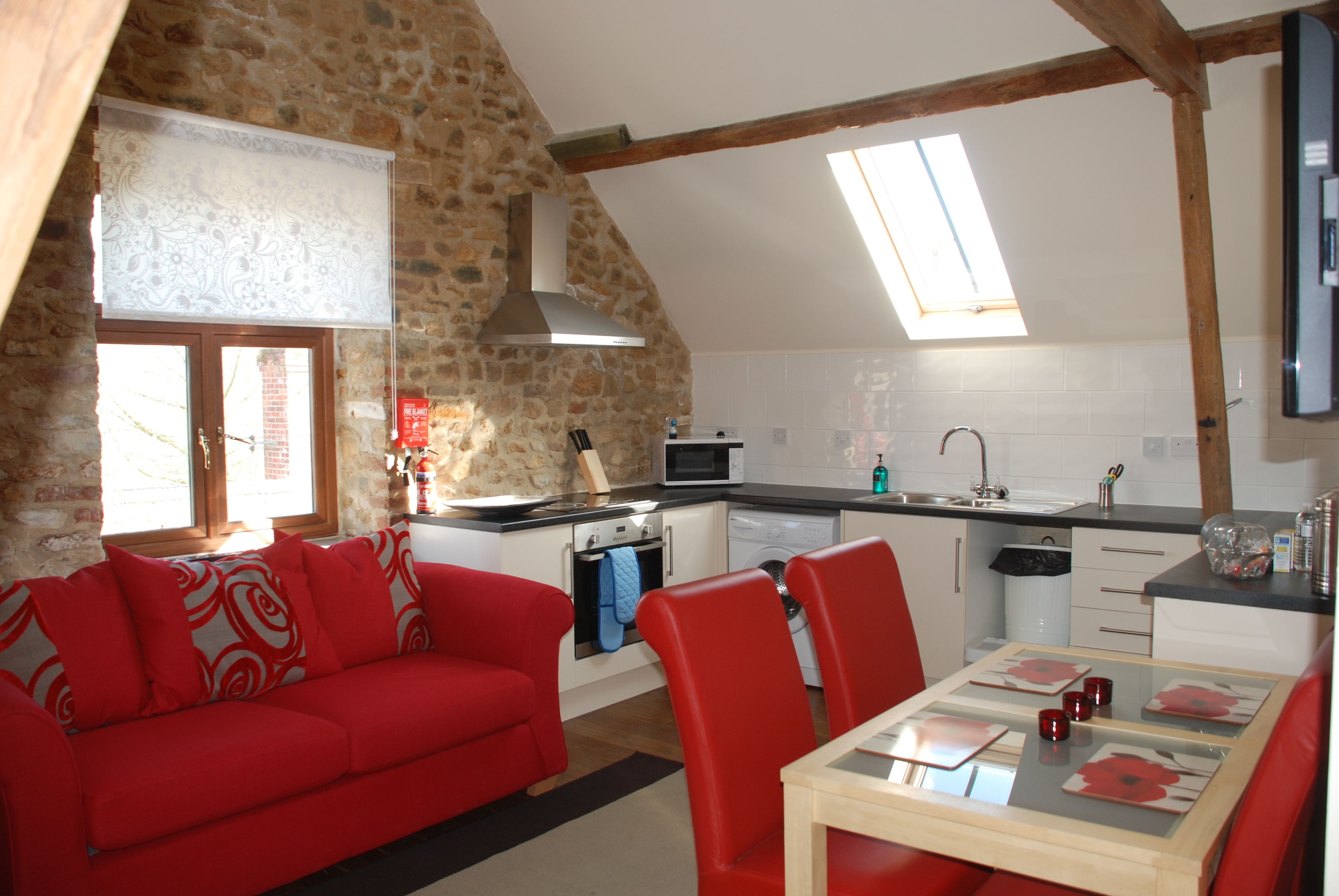 A cozy kitchen with a stone wall, a red sofa, and a dining table with red chairs.