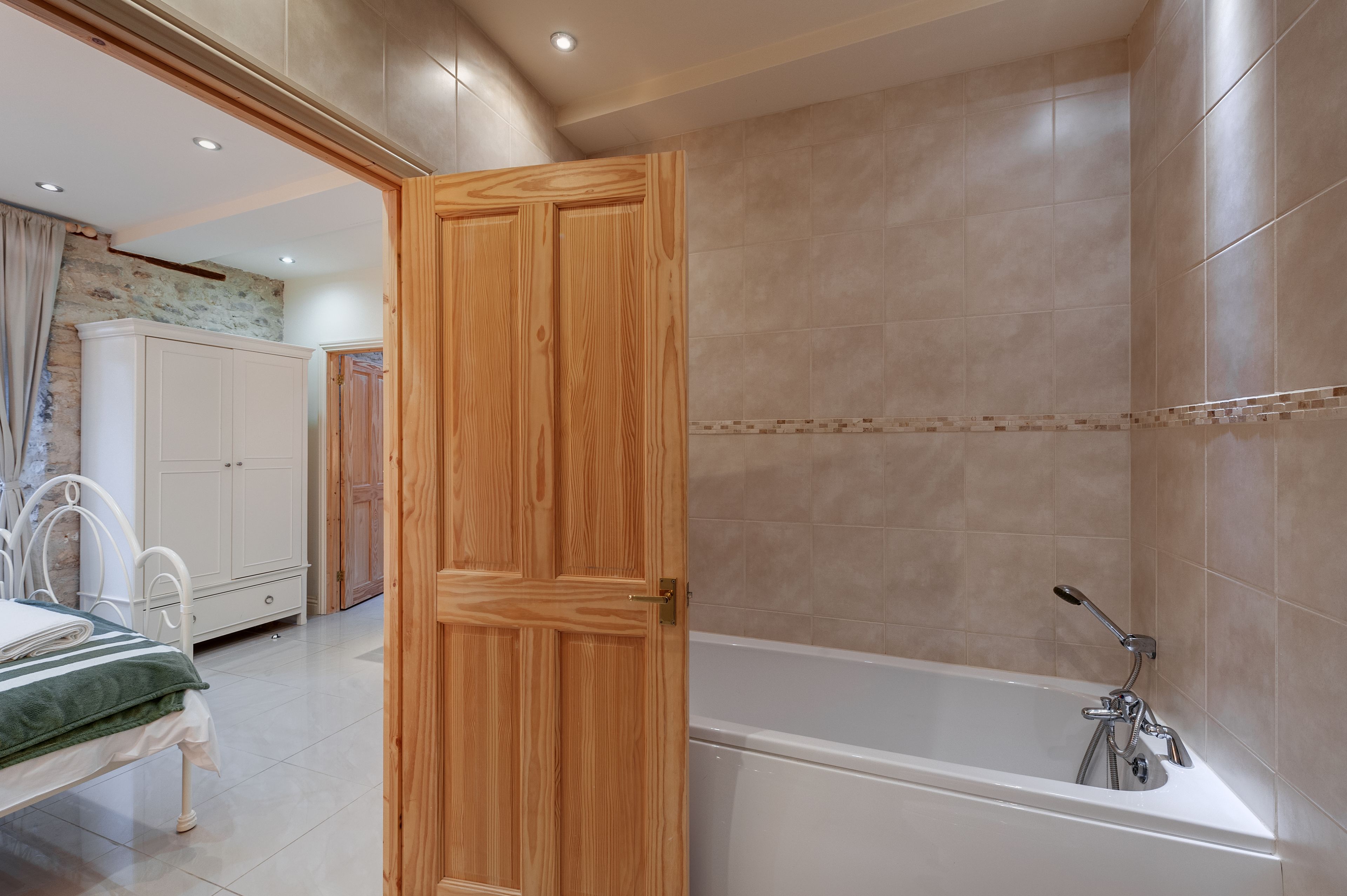 Une salle de bain moderne avec une baignoire, une porte en bois et des murs carrelés.