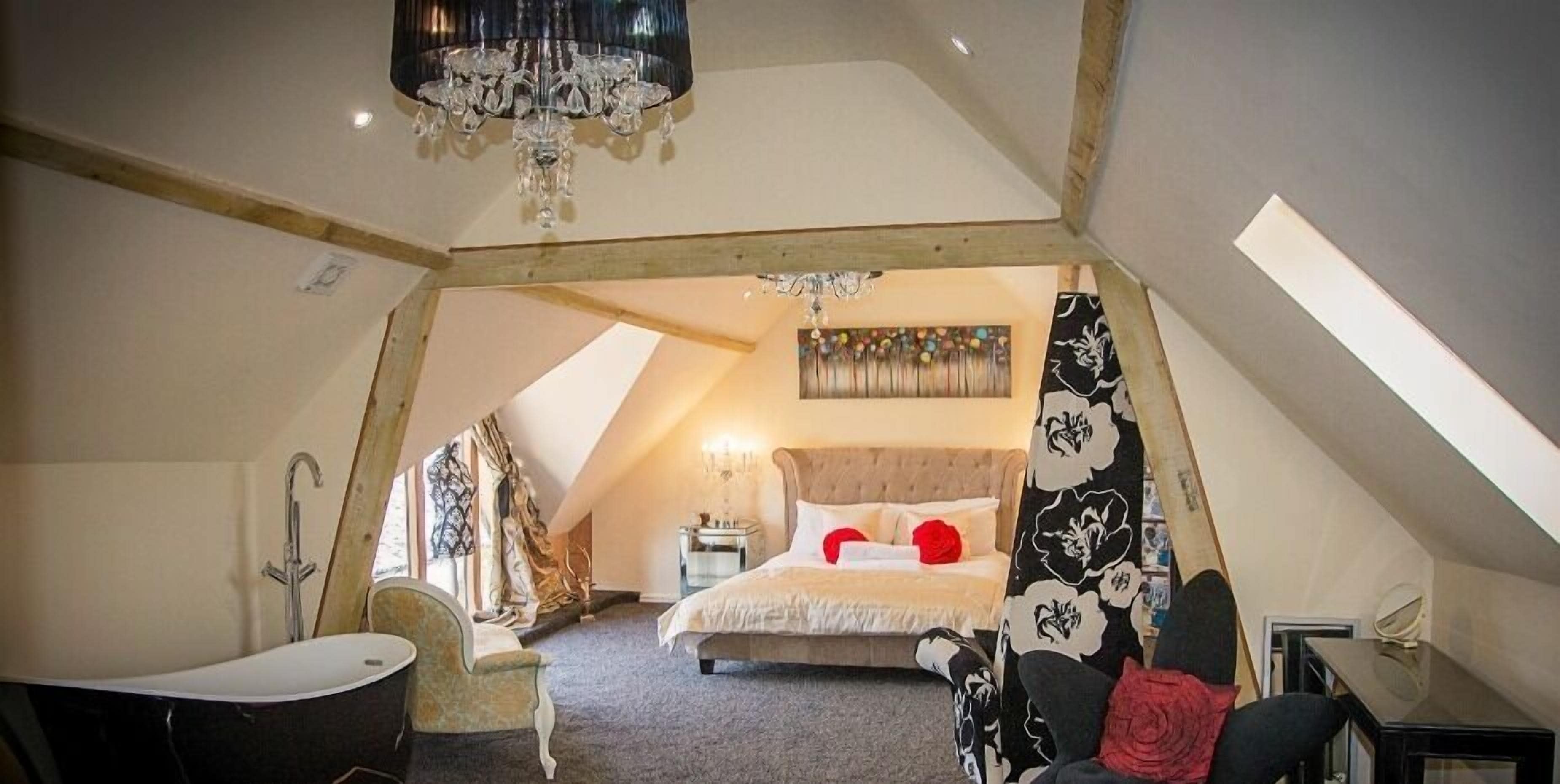 Een slaapkamer met een schuine balkenlaag, een kroonluchter, een bed, een bureau en een stoel.