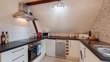 Una cocina moderna equipada con lavavajillas, horno y microondas. Se observan armarios, un fregadero y una lámpara en el techo.