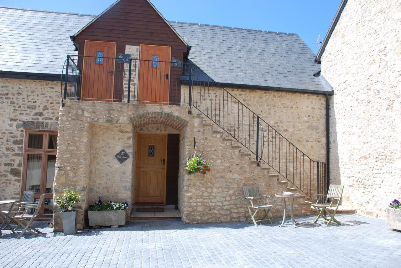 Un bâtiment en pierre avec une porte en bois, un escalier et des sièges à l’extérieur.