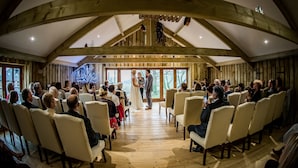 A wedding ceremony in a wooden hall with a high ceiling and natural light from large windows. - HILLS FARM STAYS (Axminster)