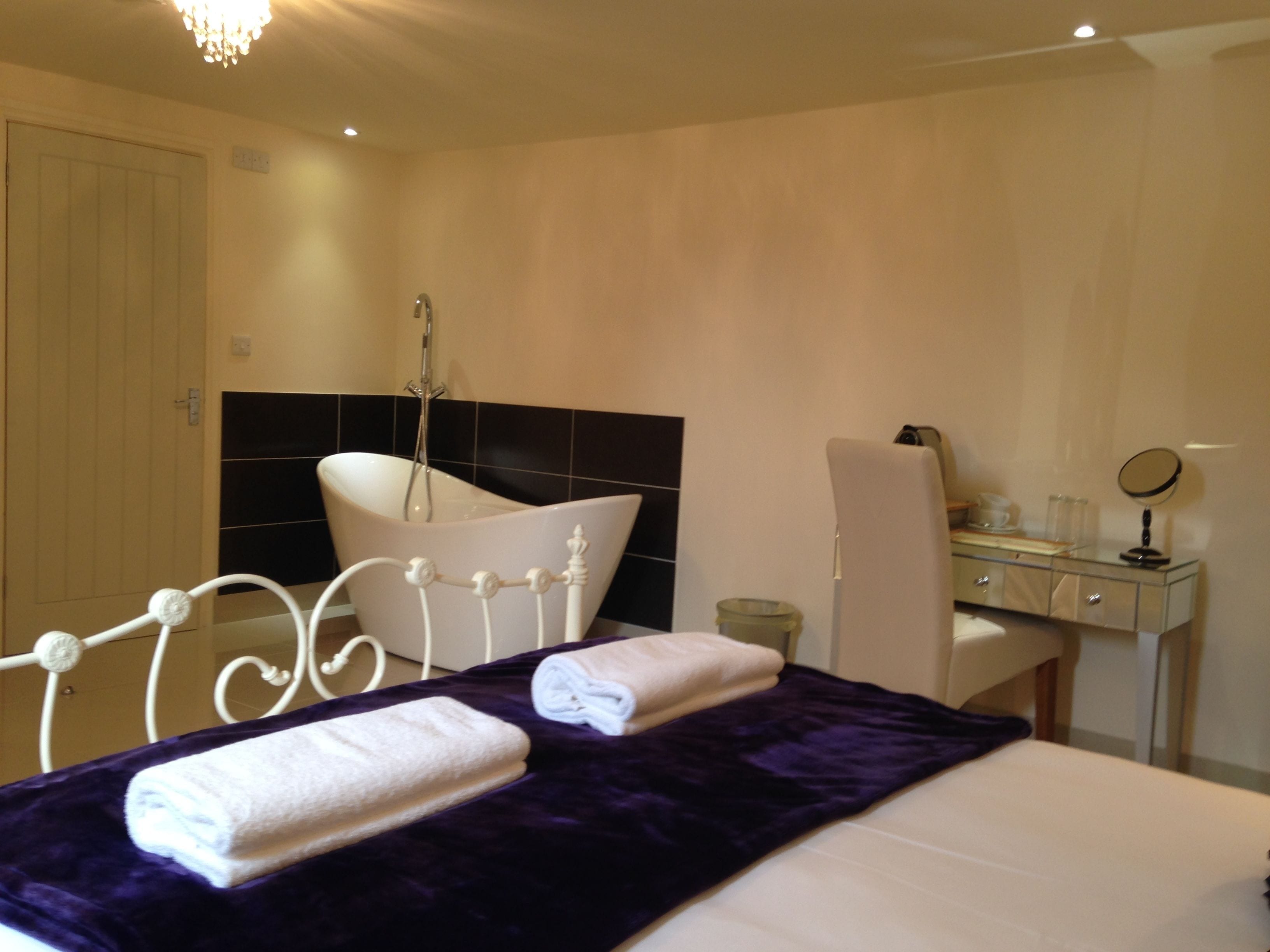 A hotel room with a bed, a bathroom with a bathtub, a desk with a mirror, and a chair.
