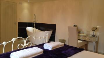 A hotel room with a bed, a bathroom with a bathtub, a desk with a mirror, and a chair.