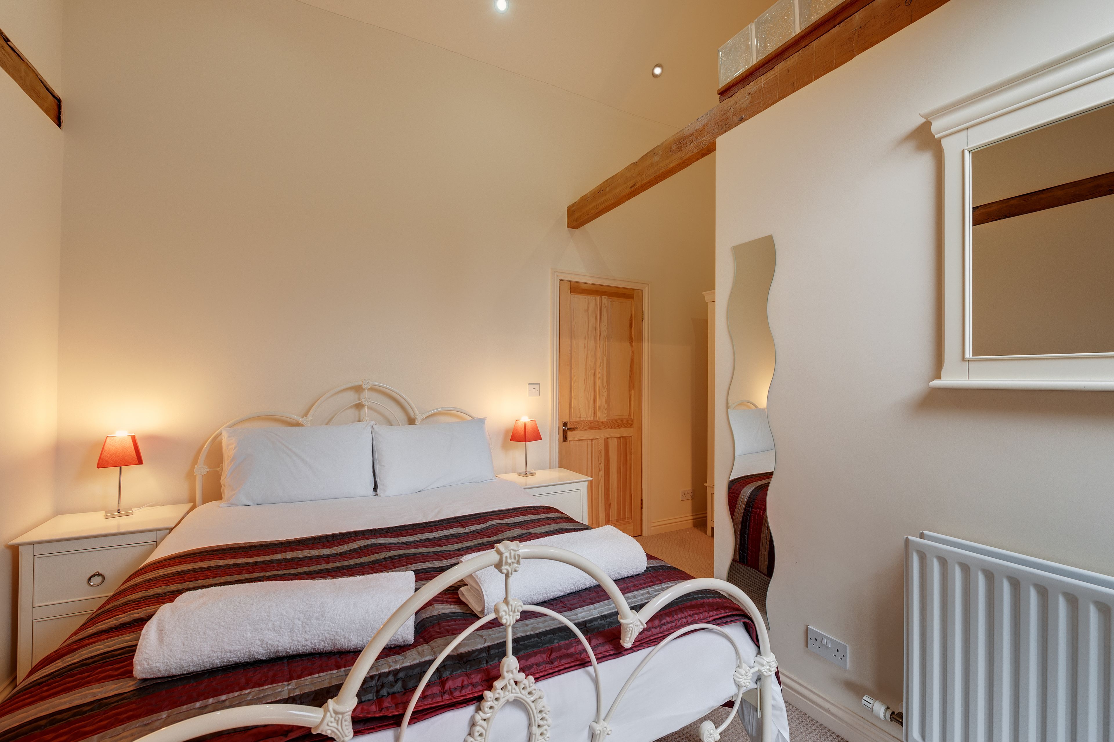 A bedroom with a bed, nightstands, a wooden door, a mirror, and a radiator.