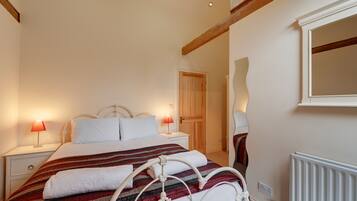 A bedroom with a bed, nightstands, a wooden door, a mirror, and a radiator.
